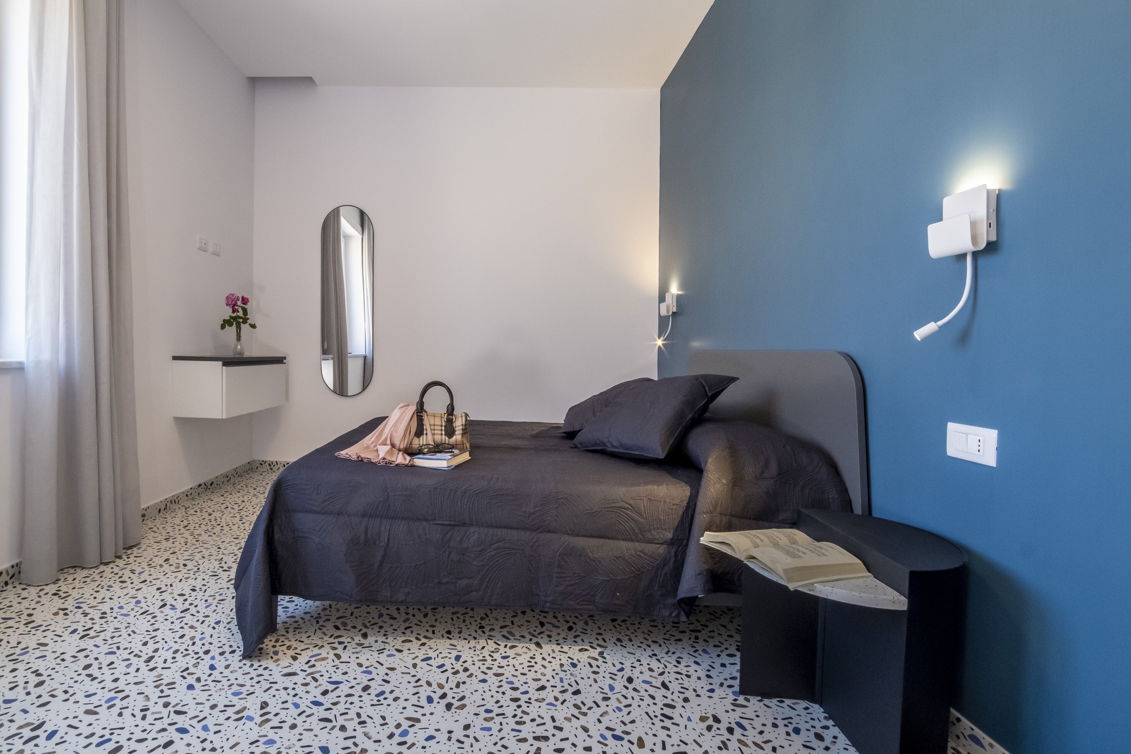 Une chambre à coucher comprenant un lit, une table de chevet, un miroir et une lampe fixée au mur.