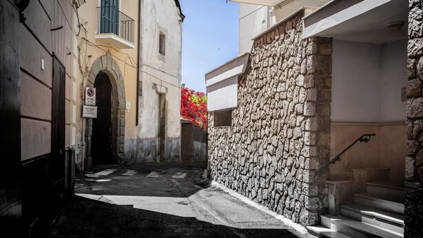 Une ruelle étroite aux murs de pierre, avec un escalier et un immeuble doté d’un balcon.