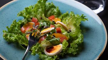 A plate of salad with a fork on a blue plate, a glass of water, and a dark background.