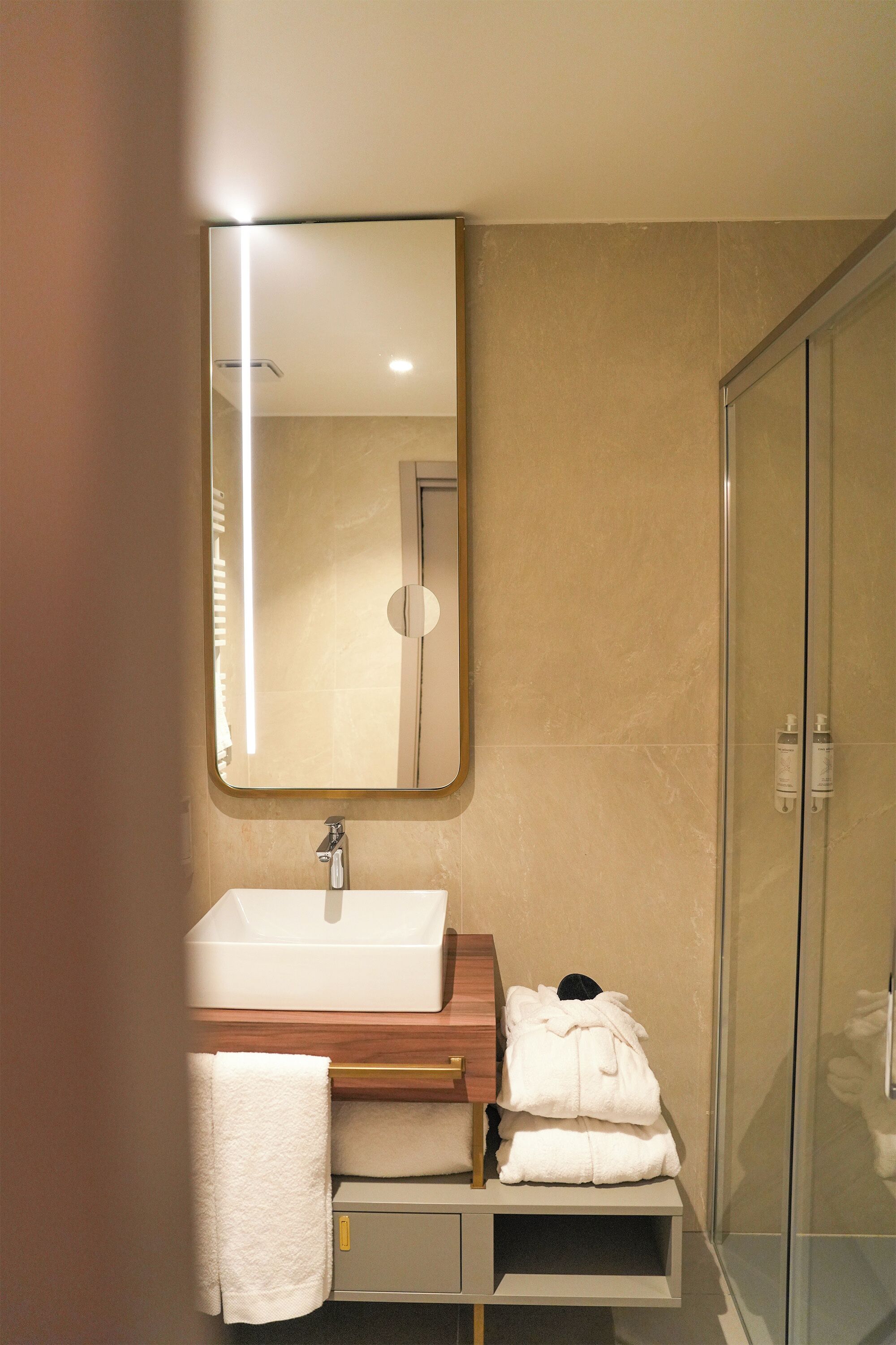 A modern bathroom with a large mirror, a sink, and a glass shower enclosure.
