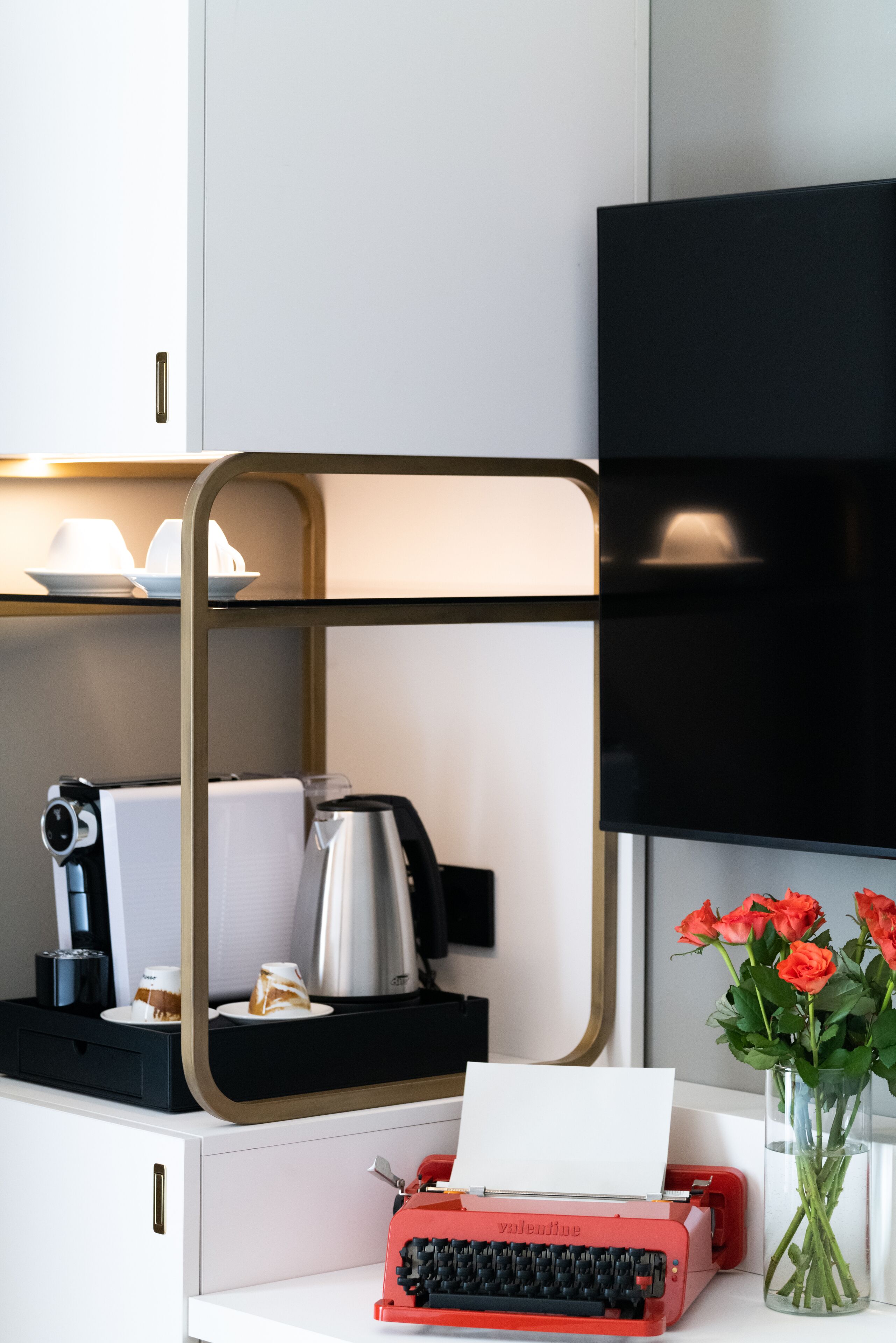 A modern kitchen with a red typewriter, a coffee machine, and a vase of flowers on the counter.