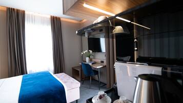 Una habitación de hotel moderna con una cama, un escritorio, una silla, una mesita con una cafetera y una ventana con cortinas.