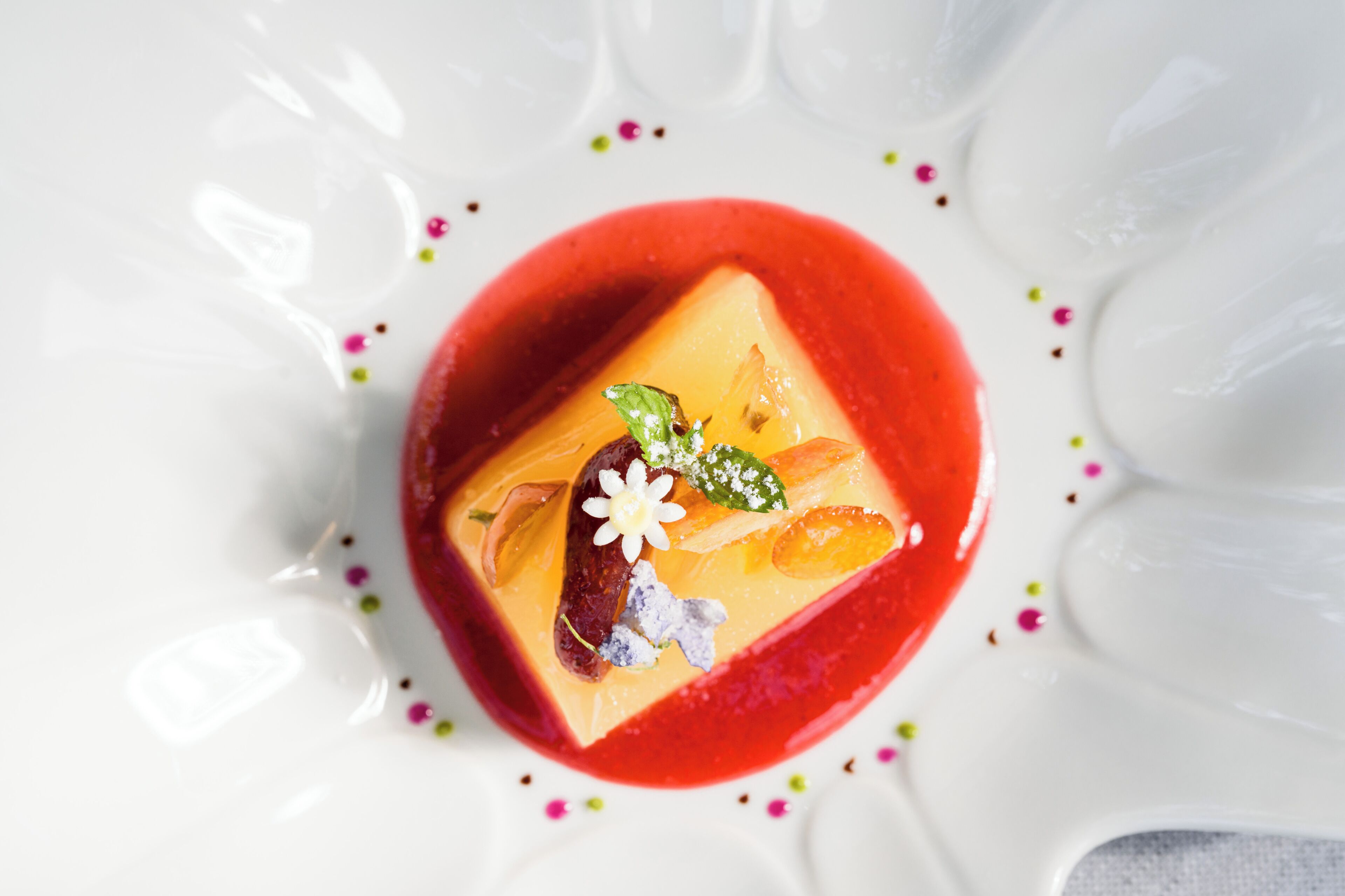 A dessert with a red sauce, a square cake, and decorative elements.