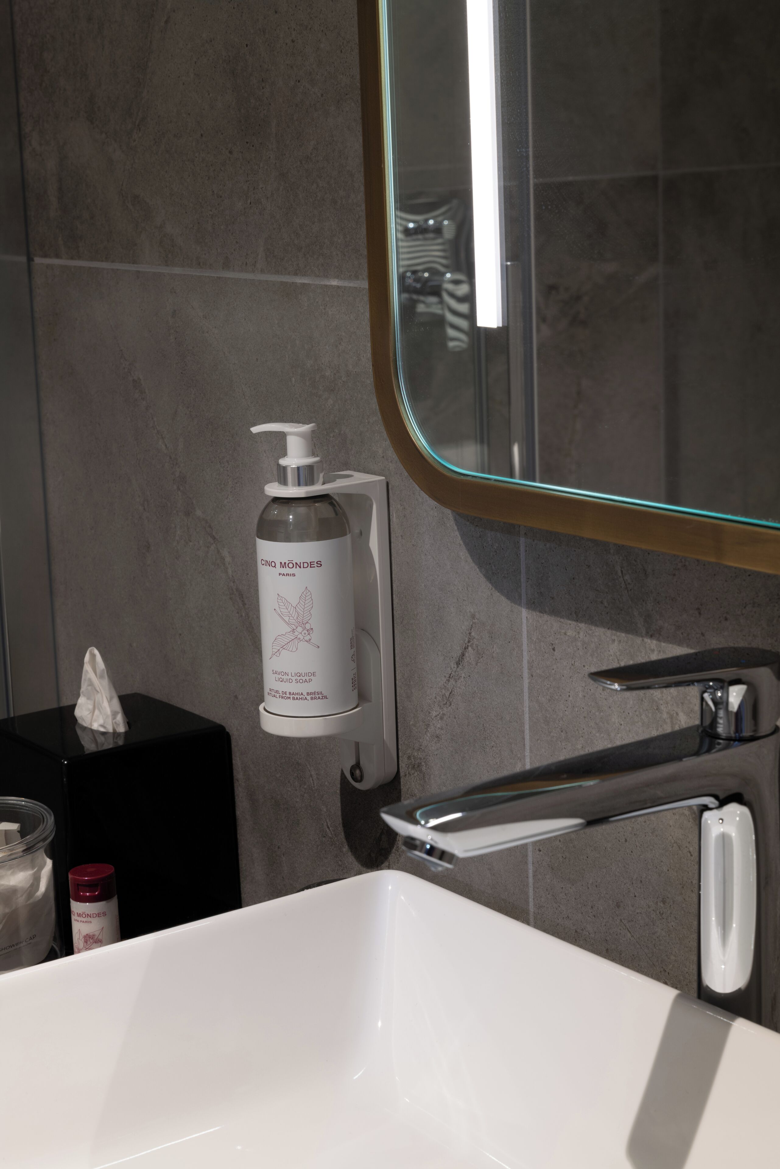 A bathroom with a white sink, a glass bottle of CNO MONDES Paris soap, and a mirror with a gold frame.