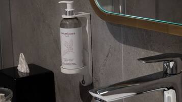 A bathroom with a white sink, a glass bottle of CNO MONDES Paris soap, and a mirror with a gold frame.