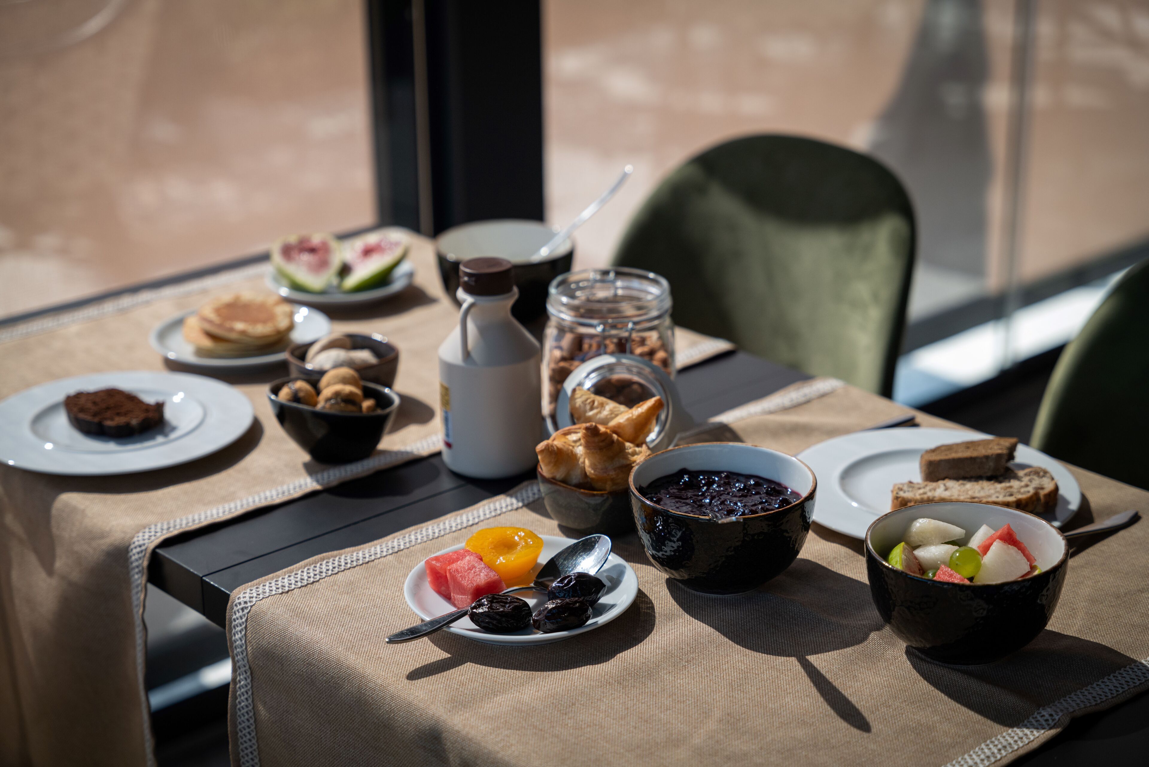 Une table dressée avec des aliments pour le petit-déjeuner, notamment des crêpes, des toasts, des fruits et du café.