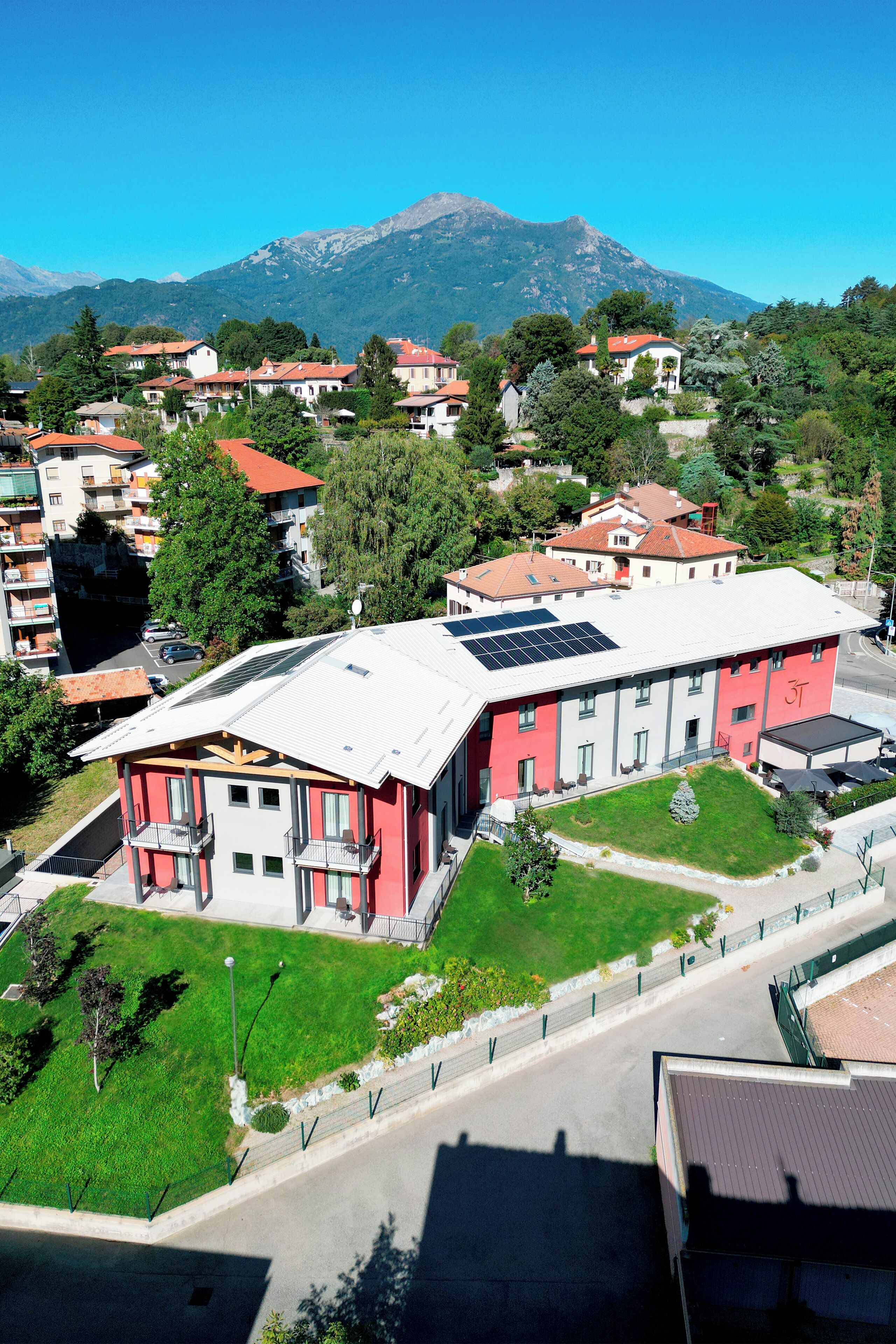 Un edifici de diversos pisos amb façana vermella, panells solars a la teulada i un jardí ben cuidat.