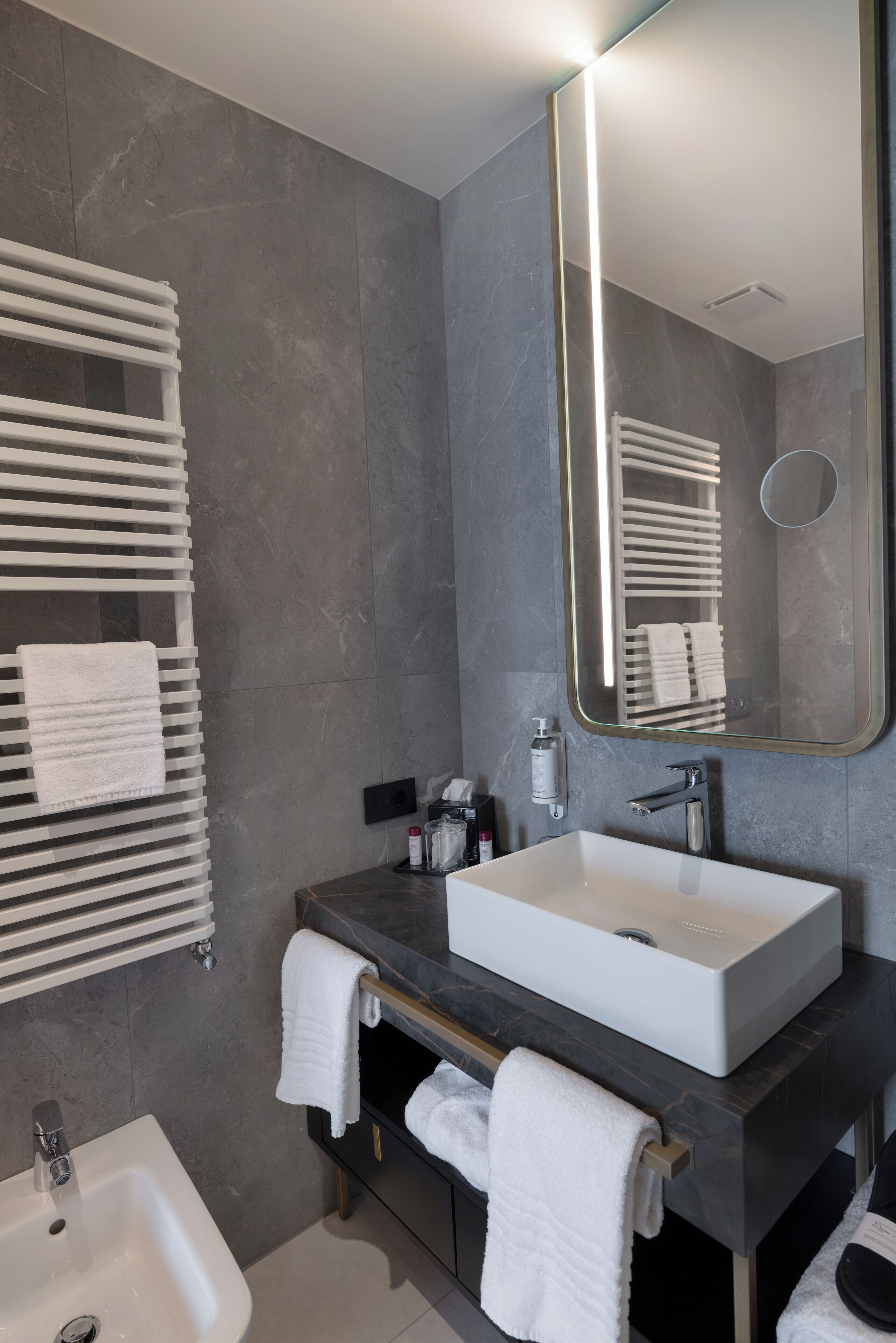 A modern bathroom with a large mirror, white sink, and towel racks.