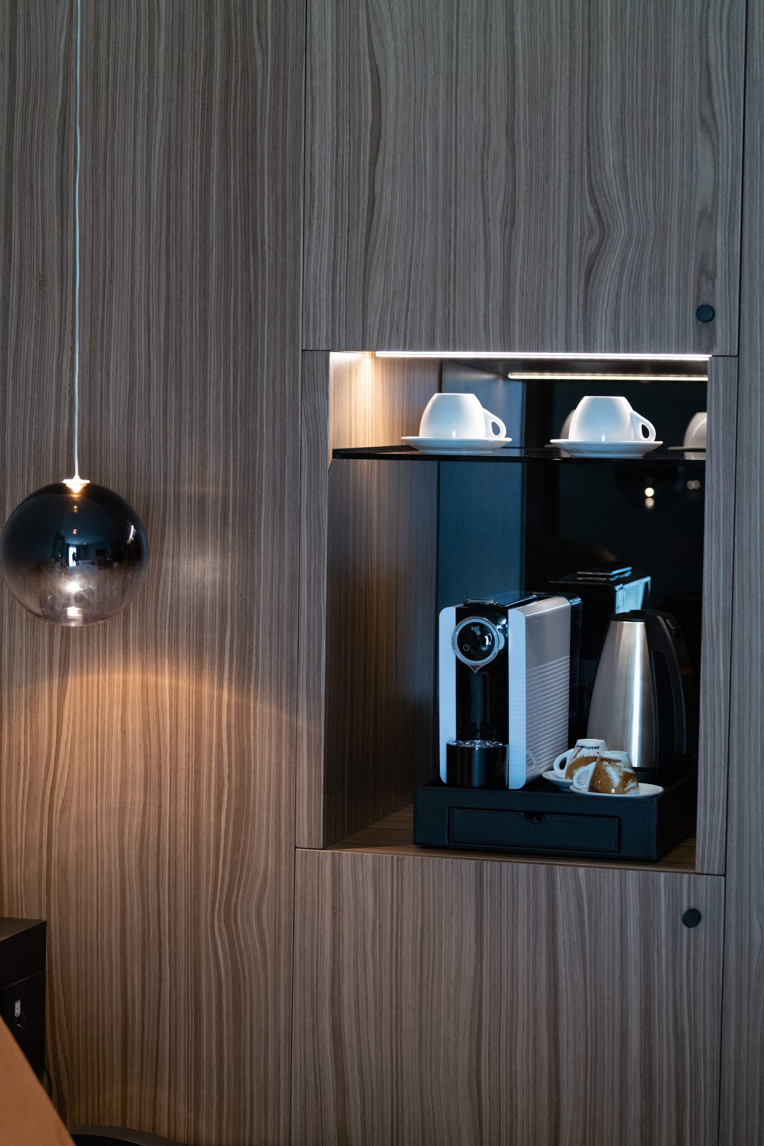 Una cafetera compacta con portavasos y jarra, montada en una pared de madera.