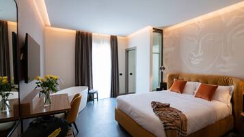 A hotel room with a large bed, a desk with a chair, a mirror, and a vase with flowers.
