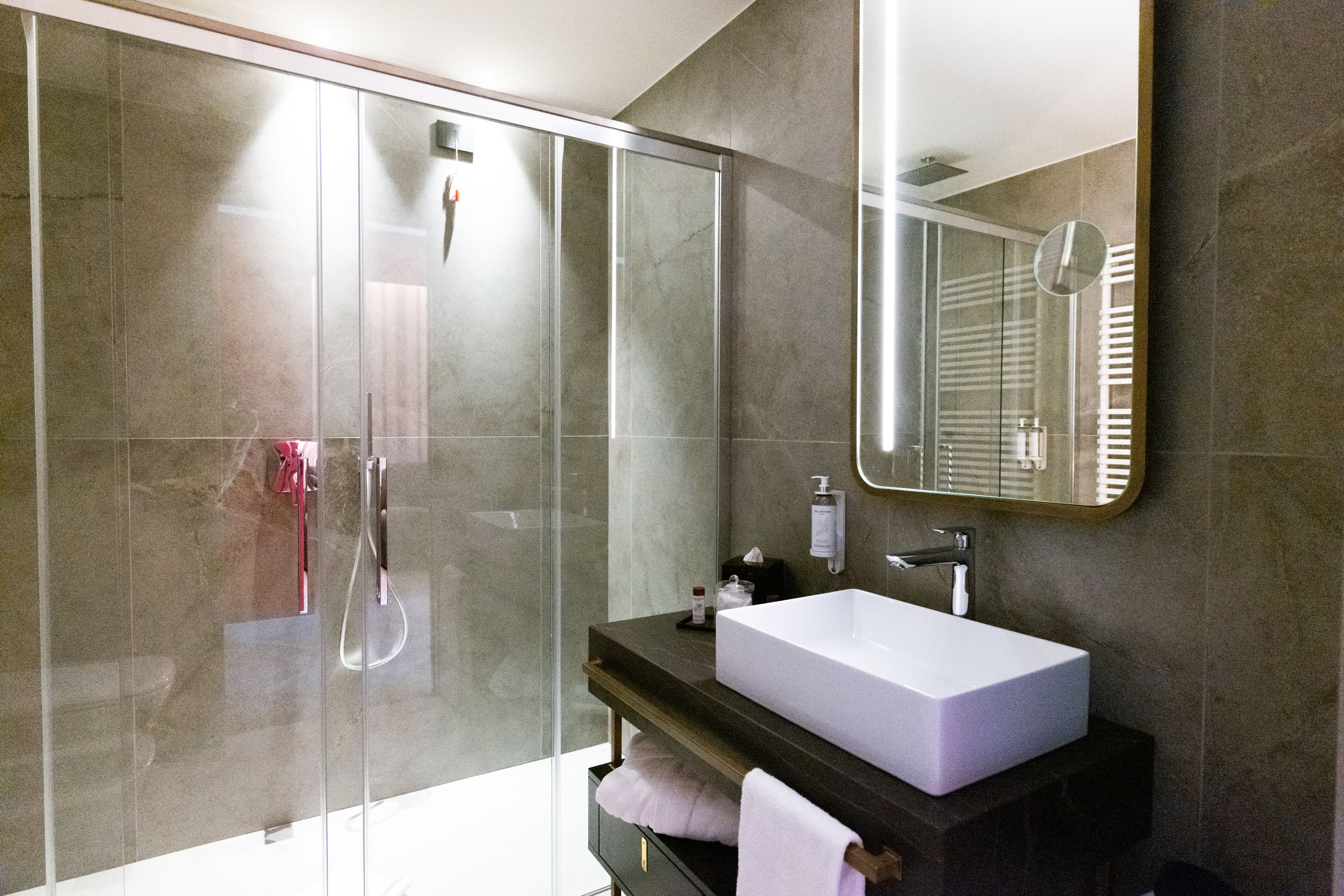 Une salle de bain moderne avec une douche à parois de verre, un grand miroir et un lavabo blanc.
