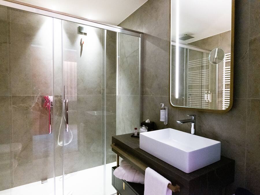 Une salle de bain moderne avec une douche à parois de verre, un grand miroir et un lavabo blanc.