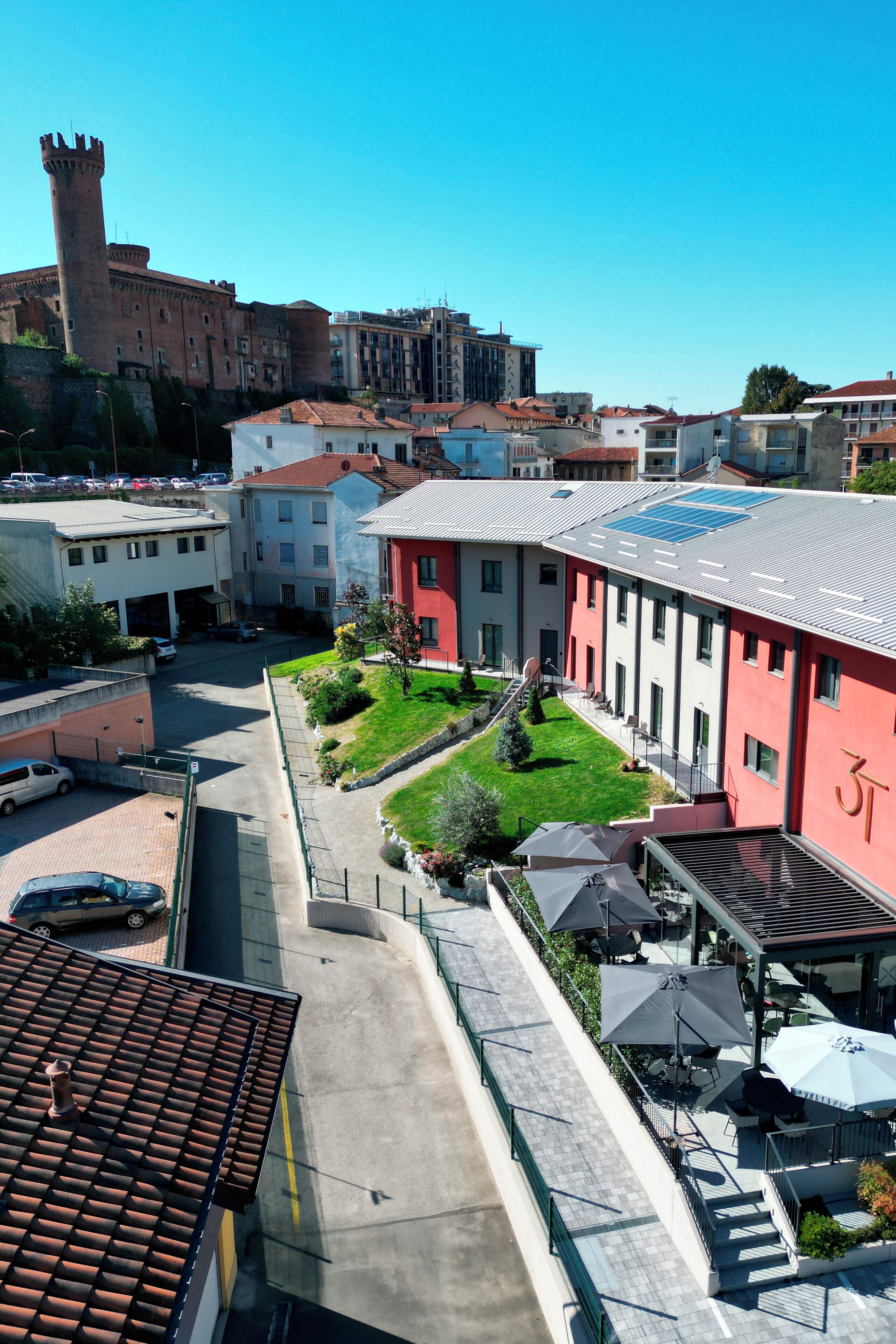 A courtyard with a red building, a tower, and a parking area.