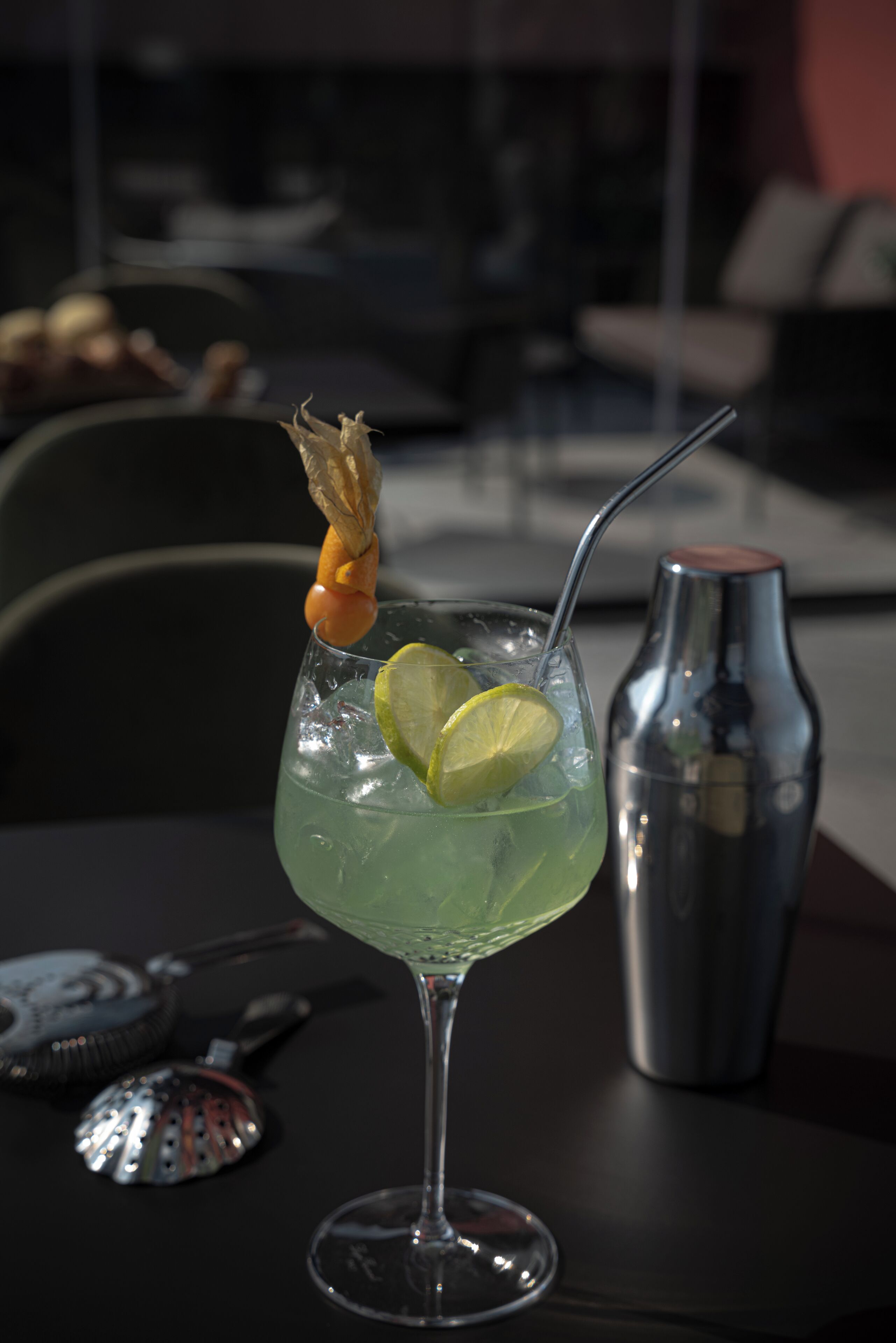 Ett cocktailglas med en limeskiva som garnering och en dekorativ frukt på ett bord.