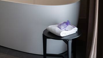 Un baño moderno con una bañera independiente, un taburete pequeño con una toalla y una cortina.