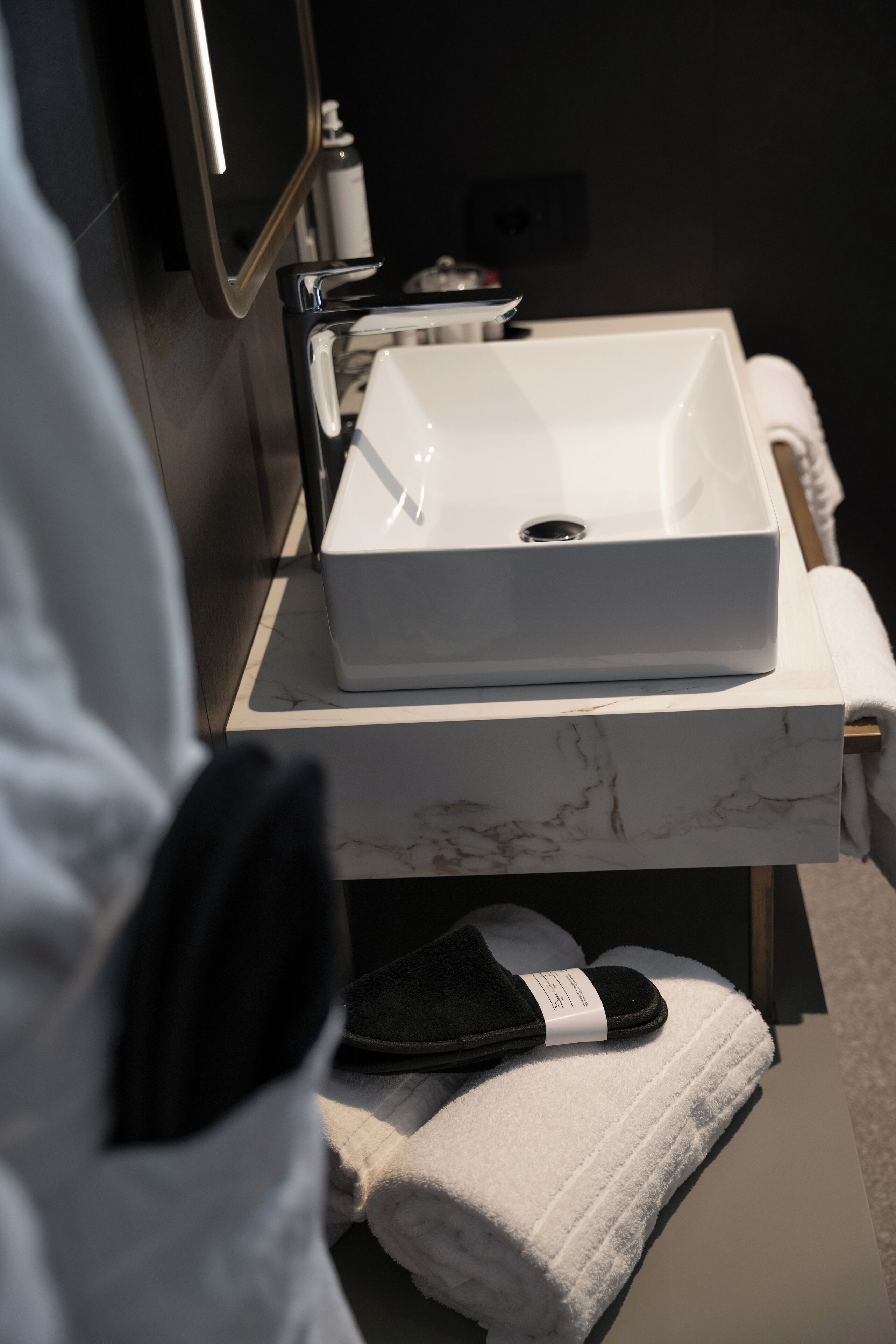 A bathroom with a white marble sink, a towel, and a pair of slippers on a shelf.