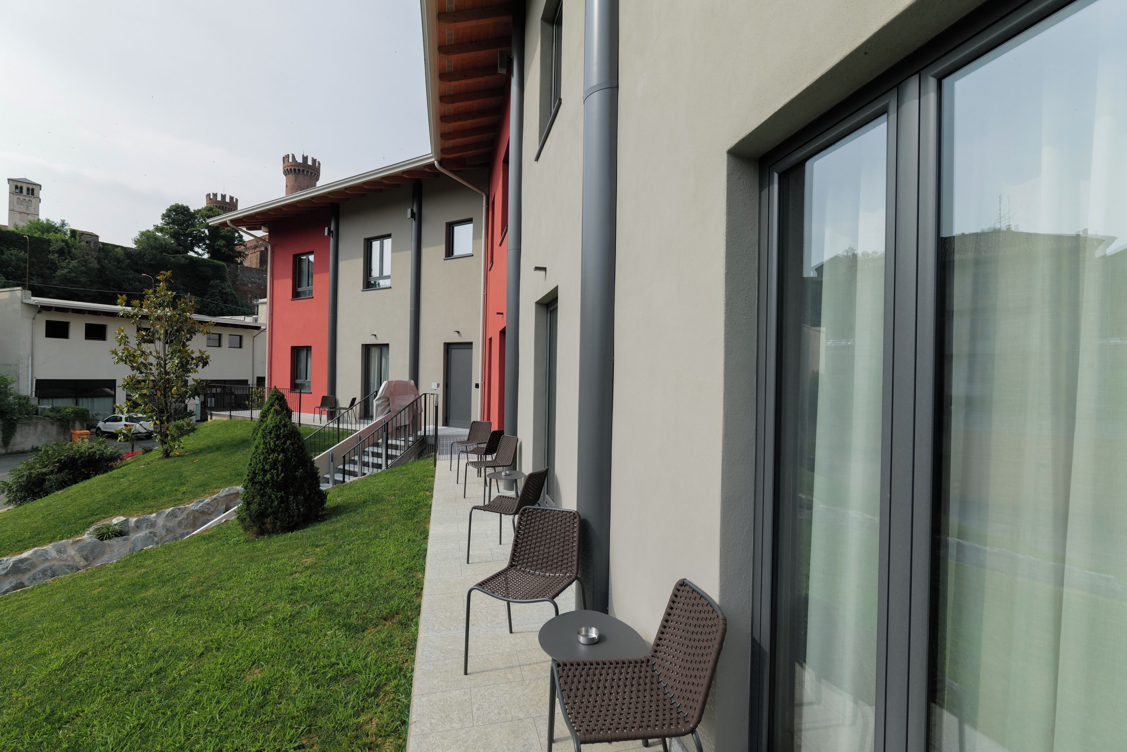 A modern building with a red facade, a balcony with chairs, and a stone pathway.