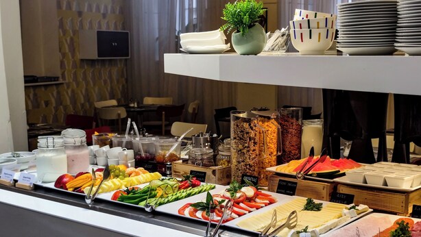 Een buffet met diverse etenswaren, waaronder fruit, groenten en vlees, gepresenteerd op schalen met bestek.