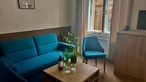 Een kamer met een blauwe bank, een houten salontafel met flessen en glazen, een stoel en een kast met een televisie.