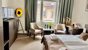 Hotelkamer met een bed, twee fauteuils, een bureau, een televisie, een lamp en een raam met gordijnen.