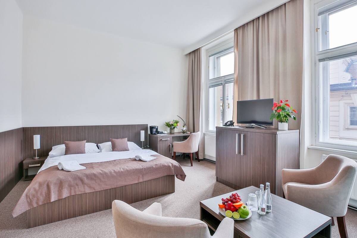 Habitación de hotel con cama, escritorio, silla, televisión y una mesa con fruta y botellas.
