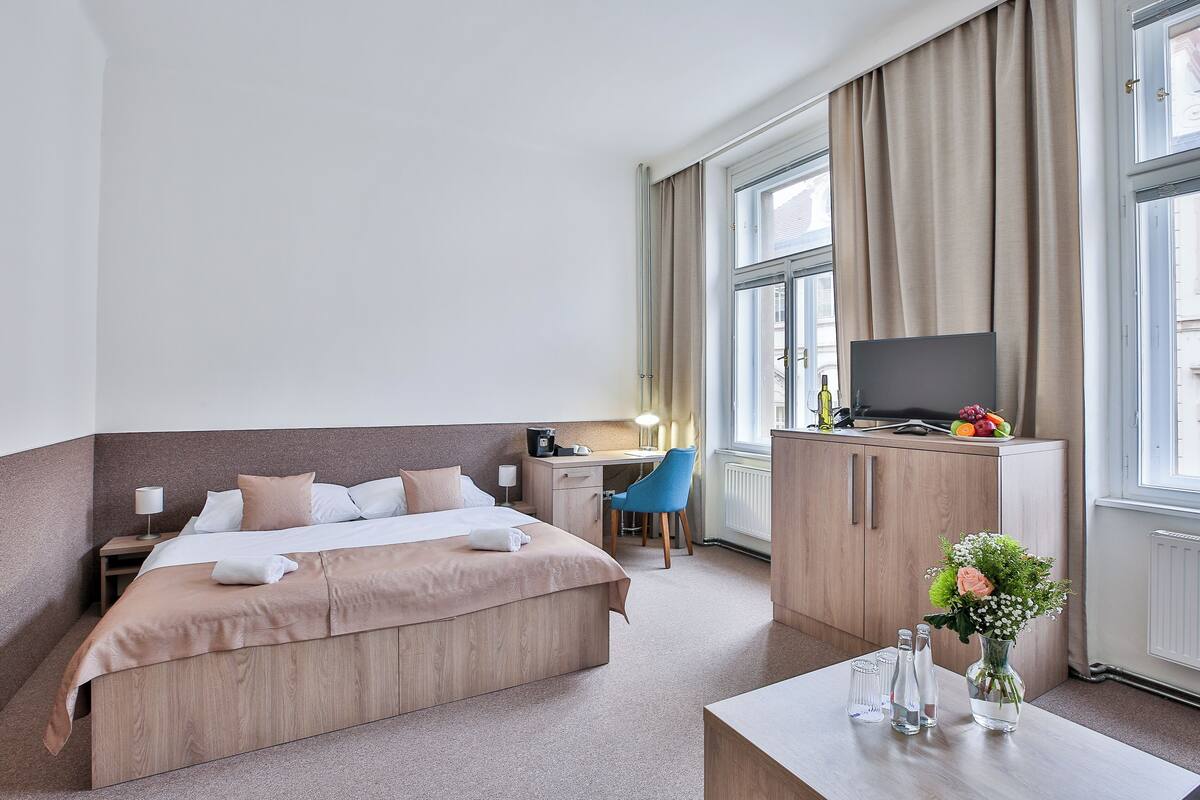 Habitación de hotel con cama, escritorio, silla, televisor y un florero con flores.
