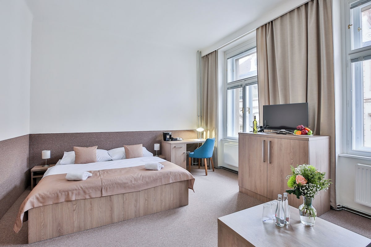 Hotellihuone, jossa on sänky, työpöytä, tuoli, televisio ja maljakko, jossa on kukkia.