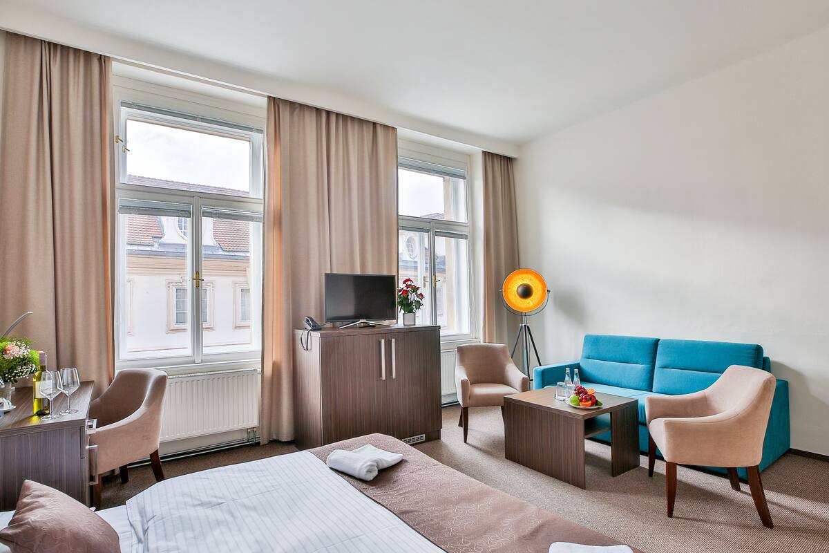 Habitación de hotel con cama, dos sillones, un sofá, un escritorio con lámpara y televisor en un mueble.