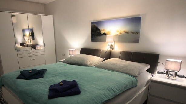 A modern bedroom with a bed, nightstands, a mirror, and a painting on the wall.