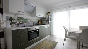A modern kitchen with white cabinets, a built-in oven, and a dining area with a table and chairs.