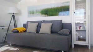 A grey sofa with three cushions, a floor lamp, and a painting of grass on the wall.