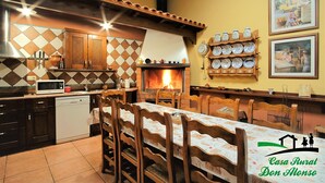 A rustic kitchen with a fireplace, wooden cabinets, and a dining area with a table set for four. - Beautiful Rural House next to the Júcar river. Rural House Don Alonso (Villalgordo del Jucar)