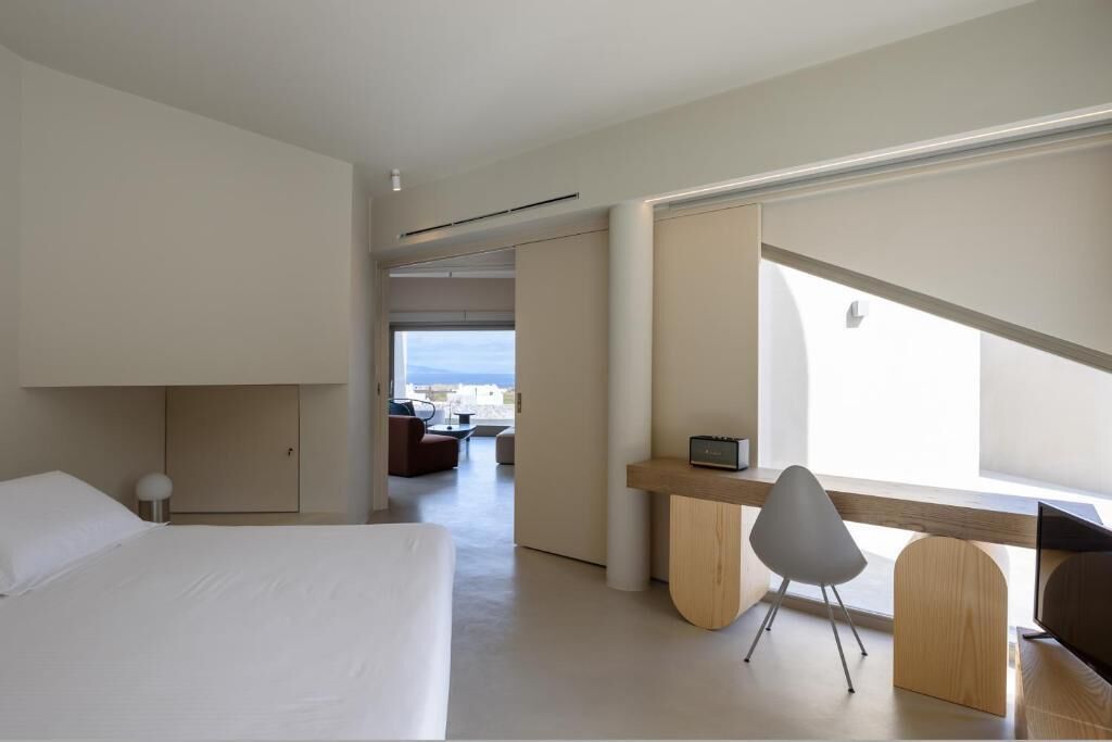 A modern hotel room with a large bed, a desk with a chair, and a view of the city.