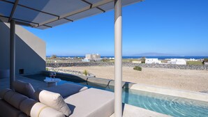 Zona junto a la piscina con un sofá color beige y una pequeña mesa, con vista a una playa y al mar.