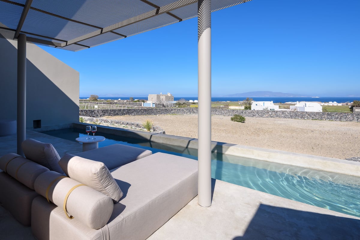 A poolside area with a beige sofa and a small table, overlooking a beach and the sea.