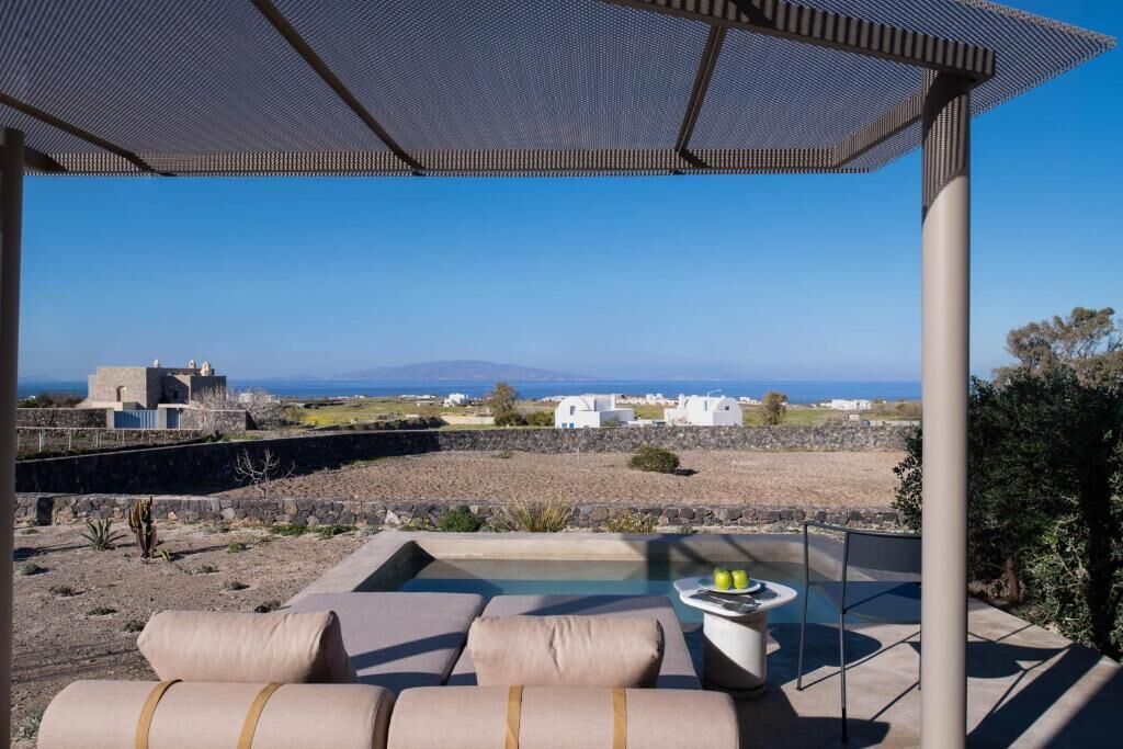 Un espace extérieur ensoleillé, aménagé avec des sièges et une piscine, offrant une vue sur un paysage côtier avec des bâtiments blancs et un ciel dégagé.
