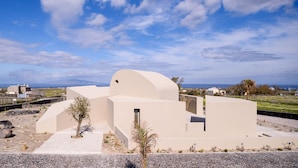 Un edificio de arquitectura moderna con fachada curva y una ventana pequeña, rodeado de un paisaje rocoso y vegetación escasa.