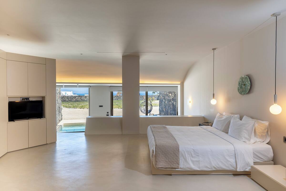 A modern bedroom with a large bed, built-in TV, and a view of the outdoors.
