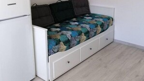 Een kleine kamer met een bed, een witte kledingkast en een Liebherr koelkast.