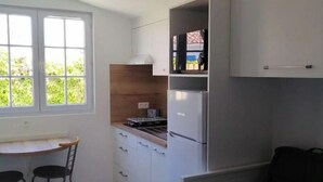 Een compacte keuken met een eethoek, een kleine koelkast, en een raam met uitzicht op groen.