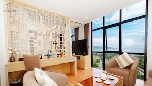 Une chambre d’hôtel moderne dotée d’un bureau en bois, d’un canapé confortable, d’une table basse et d’une grande fenêtre offrant une vue panoramique.