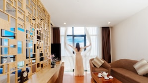 Une chambre d’hôtel avec une cloison en bois, un canapé, une table basse et une vue sur la mer à travers des rideaux transparents.
