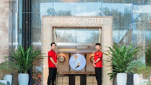 L’entrée de l’hôtel Lavencos, avec deux membres du personnel, un comptoir d’accueil et des plantes en pot.