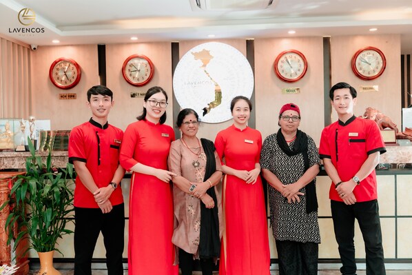 Un grupo de personal de hotel con uniformes rojos de pie en un vestíbulo con relojes y un mapa en la pared.