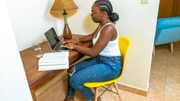 Een persoon zit aan een bureau met een laptop, een lamp en een boek.