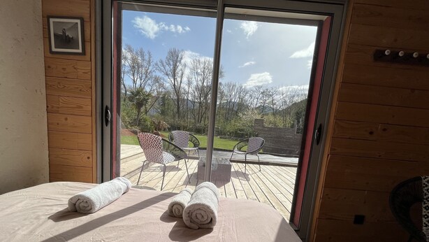 A room with a bed, two rolled towels, and a sliding glass door leading to an outdoor deck with chairs and a view of trees and mountains. - superb villa at the foot of the Pyrenees with swimming pool, large garden (Quillan)