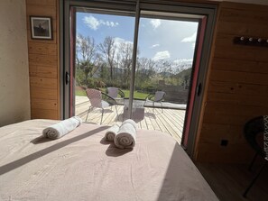A room with a bed, two rolled towels, and a sliding glass door leading to an outdoor deck with chairs and a view of trees and mountains. - superb villa at the foot of the Pyrenees with swimming pool, large garden (Quillan)