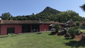 A building with a red facade and a tiled roof, surrounded by a well-maintained lawn and garden with various plants and flowers. - superb villa at the foot of the Pyrenees with swimming pool, large garden (Quillan)