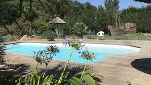 A swimming pool surrounded by lush greenery, a wooden deck, and a thatched-roof structure. - superb villa at the foot of the Pyrenees with swimming pool, large garden (Quillan)