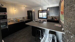 A modern kitchen with a large island, black cabinets, and a stone accent wall. - superb villa at the foot of the Pyrenees with swimming pool, large garden (Quillan)